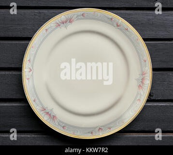 Porcelain or ceramic white plate, ordinary, with unique rose flower patterns, on top of a black wooden background tabletop Stock Photo