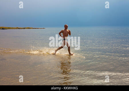 Young male athlete running at seaside in the rays of sun Stock Photo