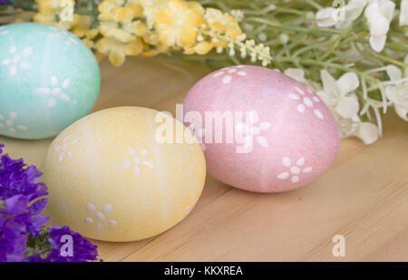 Three colored Easter eggs and flowers on a wood surface Stock Photo