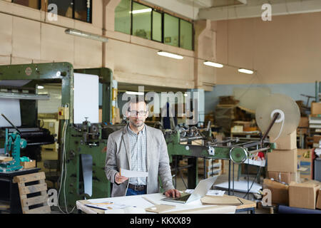 Technical engineer with paper standing by workplace and analyzing sketch in workshop Stock Photo