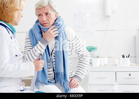 Sick senior man with scarf around neck complaining his doctor about symptoms of flu Stock Photo