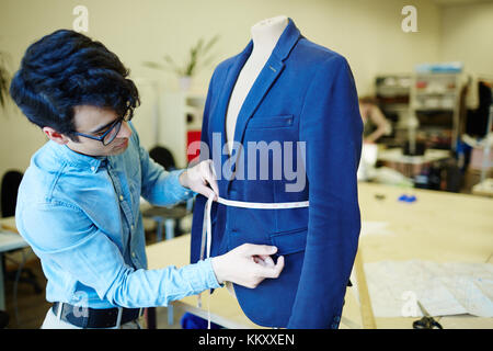 Young tailor measuring waist of blue jacket on mannequin in his workshop Stock Photo