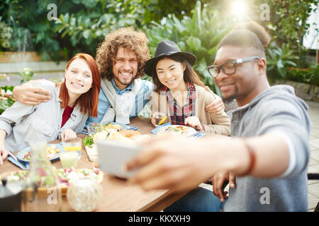 Young affectionate friends making selfie after or during dinner in garden room Stock Photo