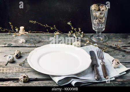 Easter table setting with vintage silverware, white plate, gray textile napkin, quail eggs and blossom branch on old wooden table Stock Photo