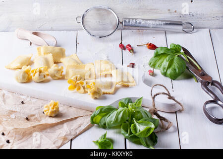 Homemade pasta ravioli and perle on white wooden table with vintage scissors, cutting board and fresh basil. See series Stock Photo