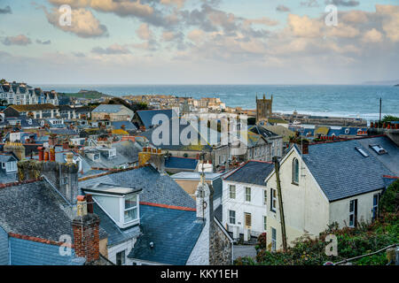 A long distance view over the rooftops of St Ives town, Cornwall. Looking out to blue sea with the harbour buildings bathed in late afternoon sunlight Stock Photo