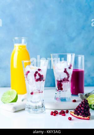 two glasses with ice and pomegranate seeds, ready for cocktails. Freshly squeezed pineapple and pomegranate juices and halves of cut lime in the backg Stock Photo