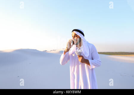 Arab young sheikh calls to friend or business partner and with smile on face and joy in eyes tells about winnings and amount of money in hands, rejoic Stock Photo