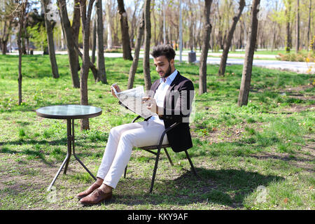 Man reading newspaper and smiling in slow motion.Muslim dressed in blue shirt and black jacket. Freelancer has dark short hair, beard and dimples on c Stock Photo