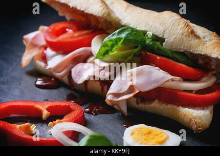 Sandwich with ham, eggs, vegetables and ketchup over black background. See series Stock Photo