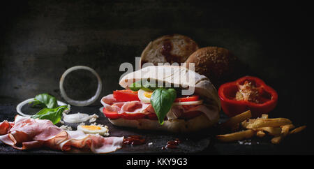 Sandwich with ham, eggs, vegetables and ketchup, served with french fries over black background. See series Stock Photo