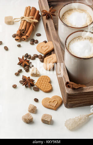 Tow cup of cappuccino served with spices and cookies as hearts on white textile Stock Photo