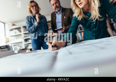 Team of architects working on construction plan. Designers working on blueprint on table in office. Focus on female hand pointing on drawing. Stock Photo