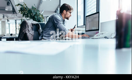 Young man sitting in office and working on desktop pc. businessman looking at computer monitor while working in office. Stock Photo