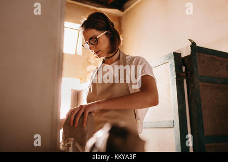 Woman kneading clay for pot making. Craftswoman preparing clay for pot making in workshop. Stock Photo