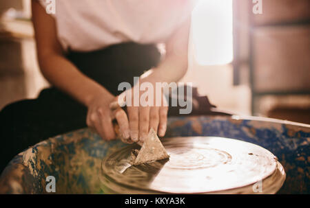 Woman potter cleaning the potters wheel using a triangular scraping tool. Craftswoman scraping clay from pottery wheel. Stock Photo
