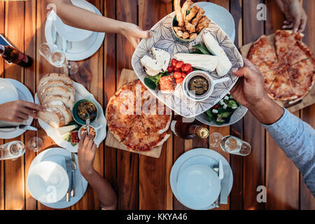 Top view of people eating meal at table served for party. Friends celebrating housewarming party on wooden table. Male hands passing food plate to fem Stock Photo