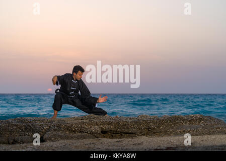 man performs tai chi moves agains sunset at the beach Stock Photo