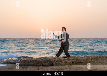 man performs tai chi moves agains sunset at the beach Stock Photo