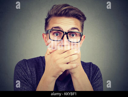 Portrait of a shocked young man covering his mouth with hands Stock Photo