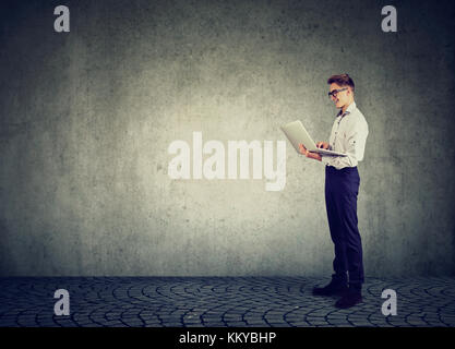 Business man using his laptop computer standing along concrete wall with blank copy space Stock Photo
