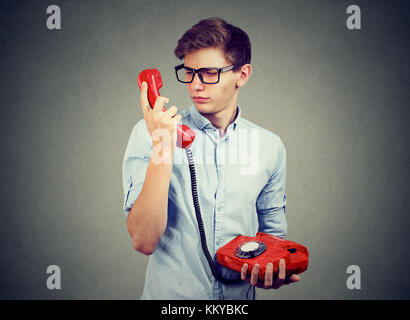 Confused worried teenager man looking at old fashioned telephone Stock Photo