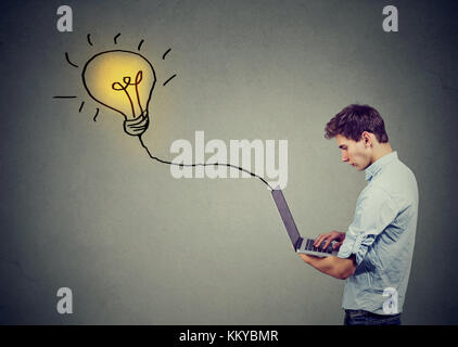 Young man using a laptop with light bulb plugged in it Stock Photo