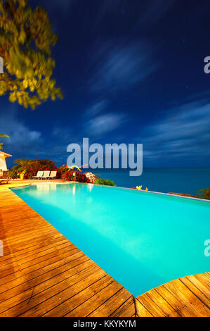 An illuminated hotel pool overlooking the Caribbean Sea at night in Antigua. Stock Photo