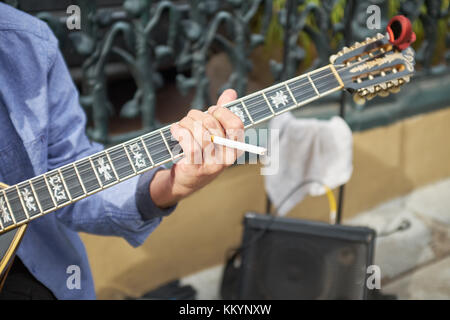 Busker smoking a cigarette as he plays his guitar outdoors on the street in a close up view of his hand Stock Photo