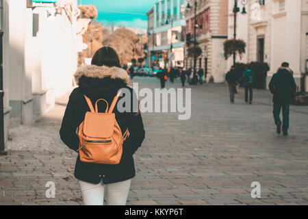 young girl with jacket and backpack walking on a town center pavement road shopping for christmas teal and orange Stock Photo