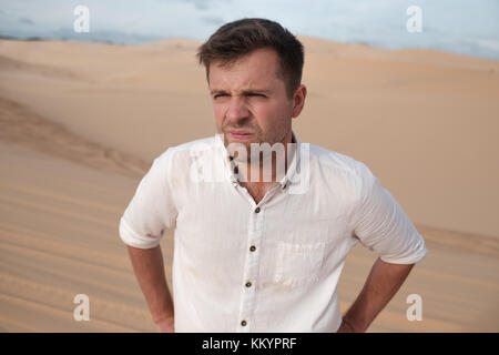 angry man with grimace on his face in desert alone. He is lost and is tired to do something Stock Photo