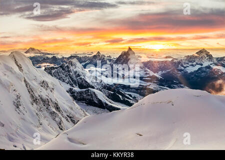 Sun setting behind the Matterhorn as seen form Monte Rosa, with mountains covered in snow Stock Photo