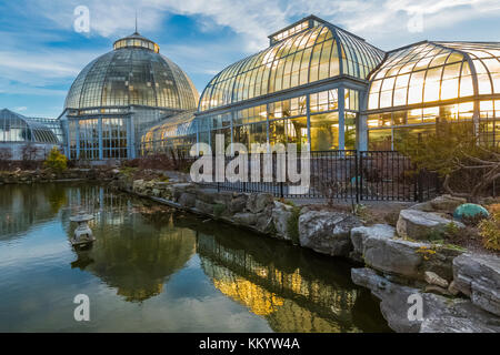 Exterior view, from the Lily Pond, of greenouses backlit by the setting sun at the Anna Scripps Whitcomb Conservatory in Belle Isle Park, Detroit, Mic Stock Photo