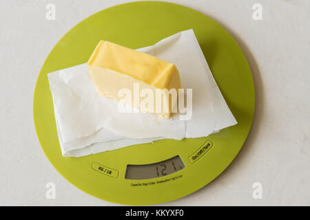 Slice of butter on greaseproof paper on digital kitchen scale Stock Photo