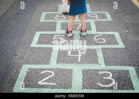 A child stands on a hopscotch, child game, board in a parking lot. Stock Photo