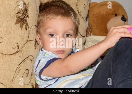 Portrait of fair-haired little boy playing with plasticine and bear home on the sofa Stock Photo