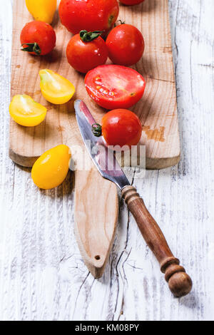 Mix of red and yellow cherry tomatoes on cutting board and vintage knife over white wooden table. See series. Stock Photo