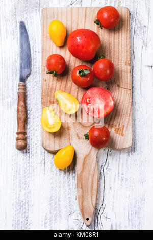 Mix of red and yellow cherry tomatoes on cutting board and vintage knife over white wooden table. See series. Top view. Stock Photo