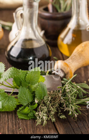 oil and vinegar in vintage bottles on wooden table, vintage knife with garlic, mint and rosemary in wooden mortar Stock Photo
