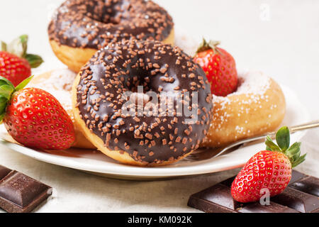 Plate with chocolate donuts, fresh strawberries and dark chocolate served on gray textile Stock Photo