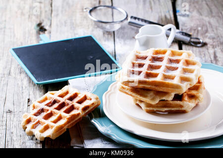 Plates with fresh belgian waffles served with empty black chalkboard over old wooden table. See series Stock Photo