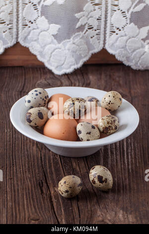 Quail and chicken eggs in white plate on old wooden table Stock Photo
