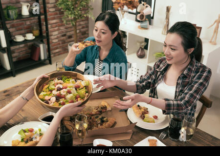 friend having dinner together and pass salad to each other in dining room at home. Stock Photo