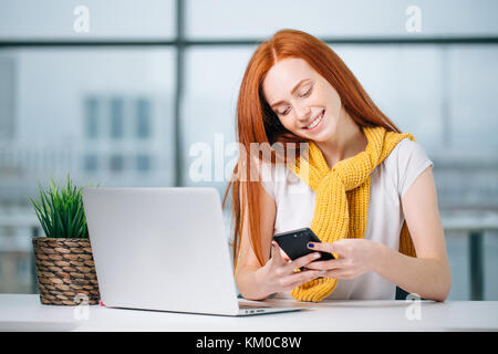 business woman sitting in office, looking at graphics and uses smartphone Stock Photo