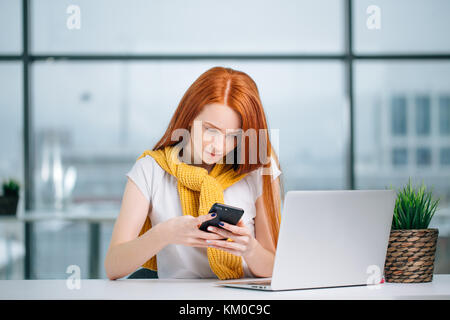 business woman sitting in office, looking at graphics and uses smartphone Stock Photo