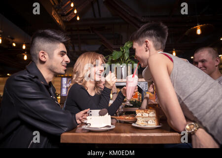 Young woman drinking milkshake while sitting with friends at cafe Stock Photo