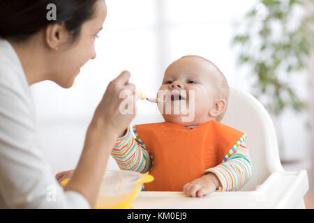 Mother feeding her baby with spoon. Mother giving healthy food to her adorable child at home Stock Photo