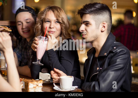 Young woman drinking milkshake while sitting with friends at cafe Stock Photo