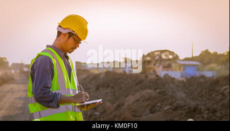 Asian engineer with hardhat using  tablet pc computer inspecting and working at construction site Stock Photo