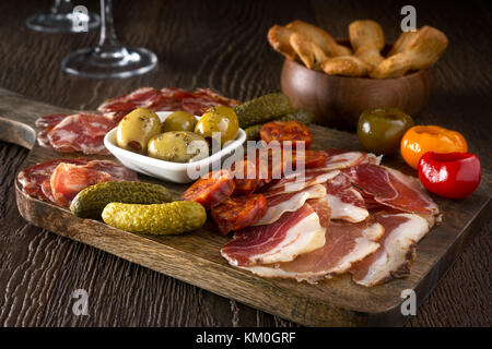 A delicious charcuterie assortment of meat, olives, gherkins, and pickled peppers with breadsticks on a wooden background. Stock Photo